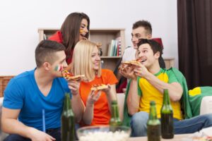 Group of multinational people eating pizza during the break in football match